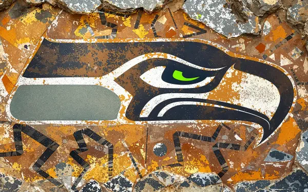 Grunge-style Seattle Seahawks logo with neon green eye on a rusted orange and gray textured backdrop — 4K Ultra HD PC desktop wallpaper and background.