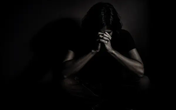 4K Ultra HD PC desktop wallpaper of a solitary figure in darkness, head bowed and hands clasped, conveying isolation and depression.