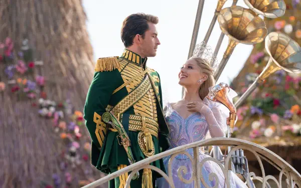 4K Ultra HD PC desktop wallpaper from Wicked: For Good — Prince Fiyero in ornate green uniform gazes at his partner in a pastel ballgown on a decorative balcony, romantic film still.