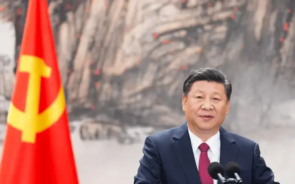 Portrait of a suited man at a podium beside a red hammer-and-sickle flag, ink-mountain backdrop — 2K Quad HD PC desktop wallpaper.