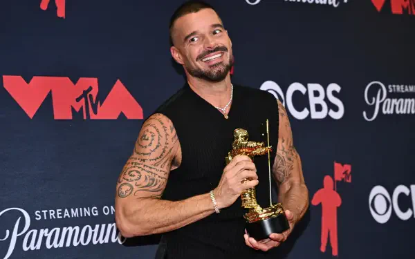 Celebrity musician (identity not disclosed) smiles holding an MTV Video Music Awards Moon Person trophy against a branded backdrop — 2K Quad HD PC desktop wallpaper/background.