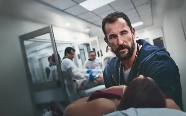 The Pitt — 4K Ultra HD PC desktop wallpaper: tense hospital corridor scene with a bearded man leaning over an injured patient on a gurney while hazmat-suited staff work in the background.