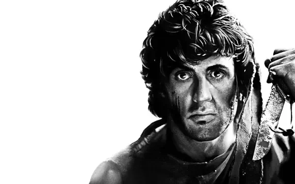 Black-and-white 4K Ultra HD desktop wallpaper: grim, battle-worn action hero with a bandana and knife, intense glare against a stark white background.