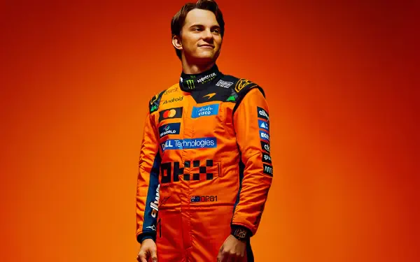 Person in orange McLaren F1 racing suit with sponsor logos on matching orange background — 2K Quad HD PC desktop wallpaper.