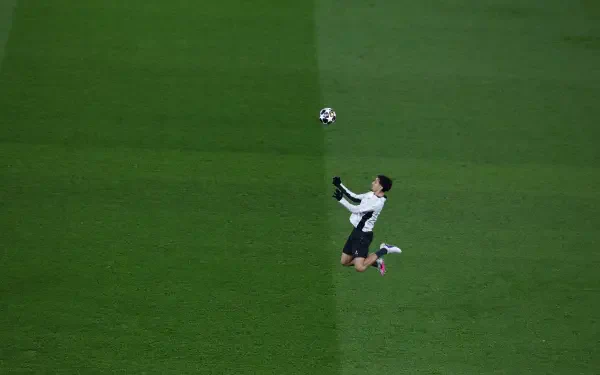 4K Ultra HD desktop wallpaper: overhead shot of a Paris Saint-Germain F.C. player leaping to head the ball during a UEFA Champions League match on a vivid green pitch.