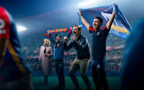 Ted Lasso and coaches cheer on a floodlit soccer pitch, scarf raised; 4K Ultra HD PC desktop wallpaper and background.