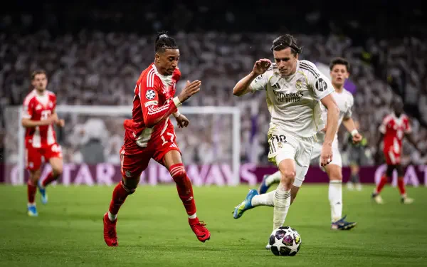 4K Ultra HD desktop wallpaper: soccer action — FC Bayern Munich player in red races a Real Madrid player in white for the ball on a packed stadium pitch.