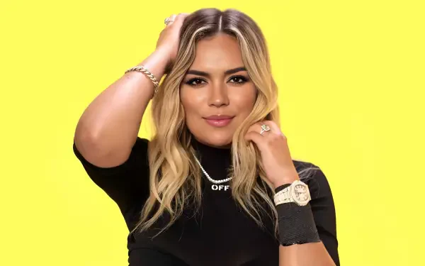 Close-up portrait of a blonde reggaeton singer celebrity against a vivid yellow backdrop, styled as a 4K Ultra HD PC desktop wallpaper.