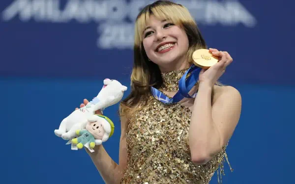 Smiling female figure skater holding a gold medal and plush mascot at the Winter Olympics, ice skating sports scene rendered as a 2K Quad HD desktop wallpaper.