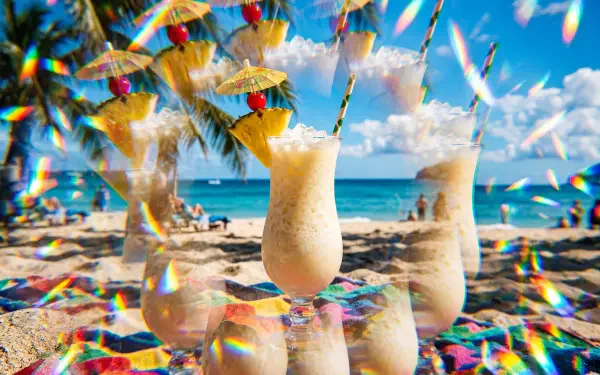 Pina Colada glasses on a sunlit tropical beach with parasols and prism light flares — 5K Ultra HD PC desktop wallpaper/background.