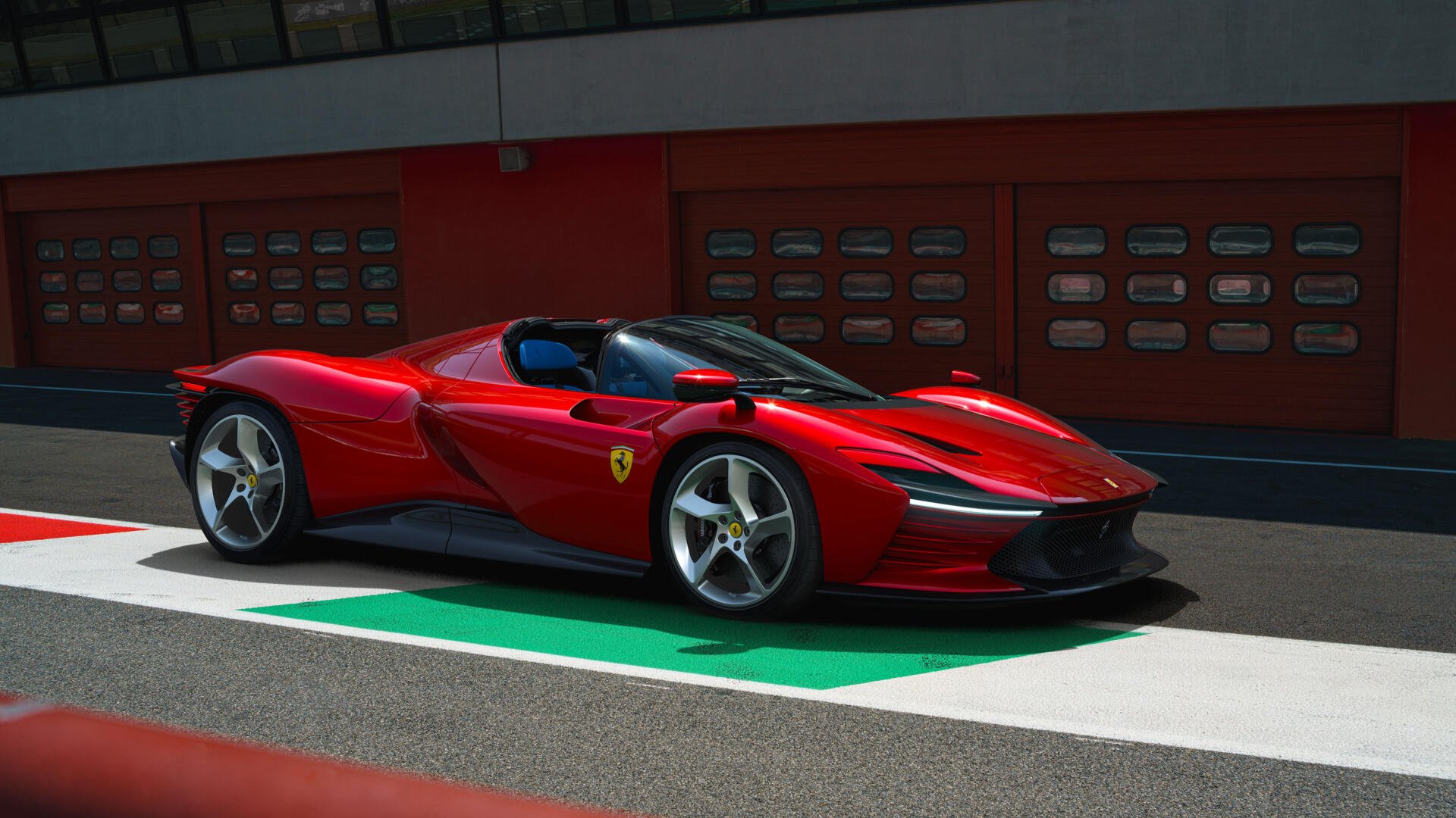 Red Ferrari Daytona SP3 vehicle on a racetrack pit lane, rendered as a 2K Quad HD PC desktop wallpaper background.
