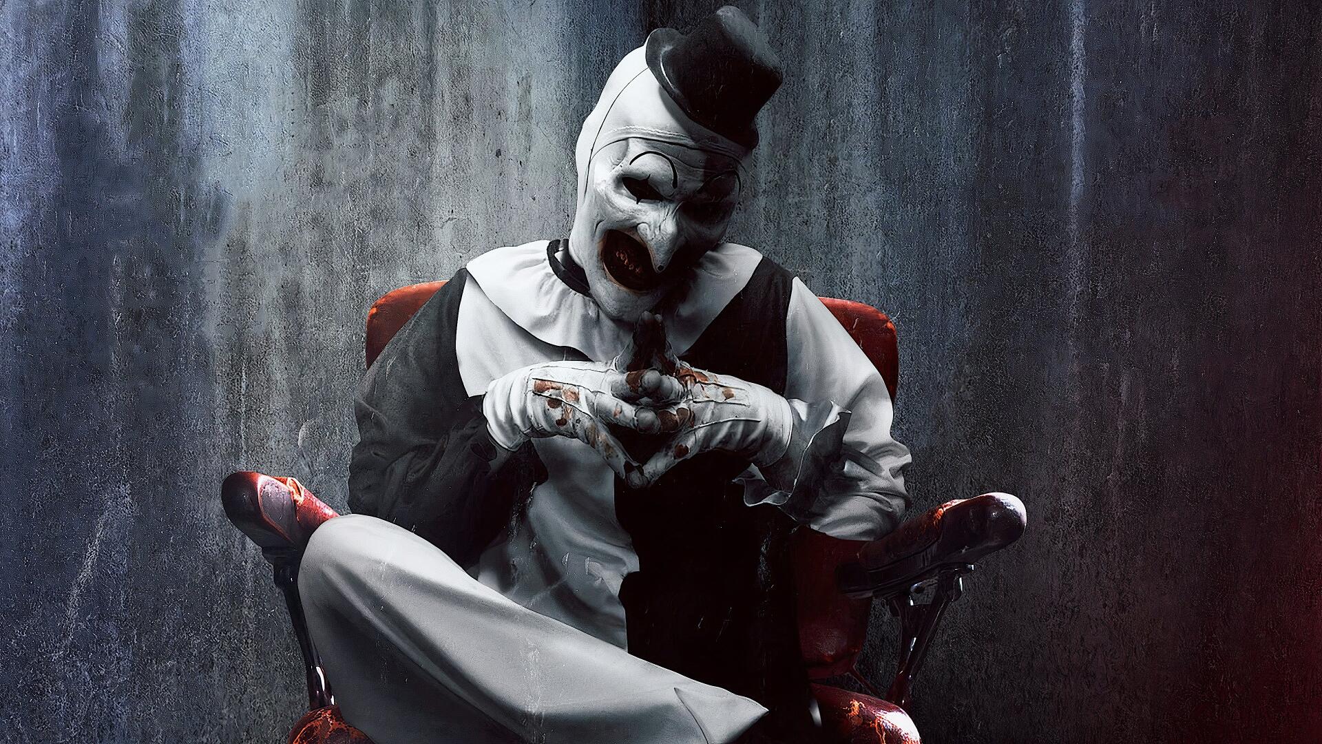 Terrifier 2 4K Ultra HD PC wallpaper: menacing Art the Clown in white makeup and black hat, seated in a red chair, steepling blood-stained fingers against a rain-streaked concrete wall.