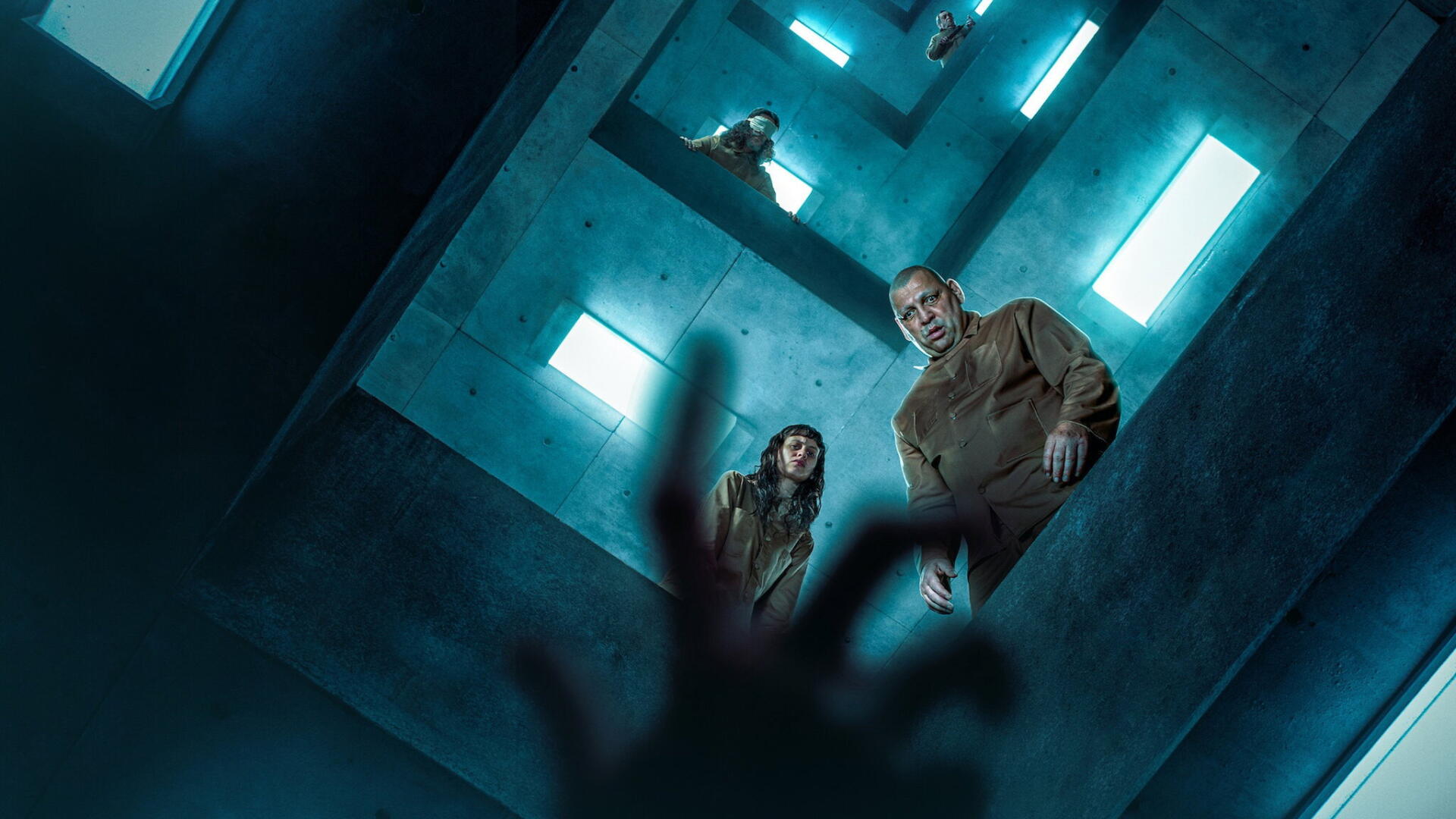 El Hoyo 2 HD PC desktop wallpaper and background: view up a concrete vertical shaft with two figures peering down through illuminated levels while shadowed hands reach upward.