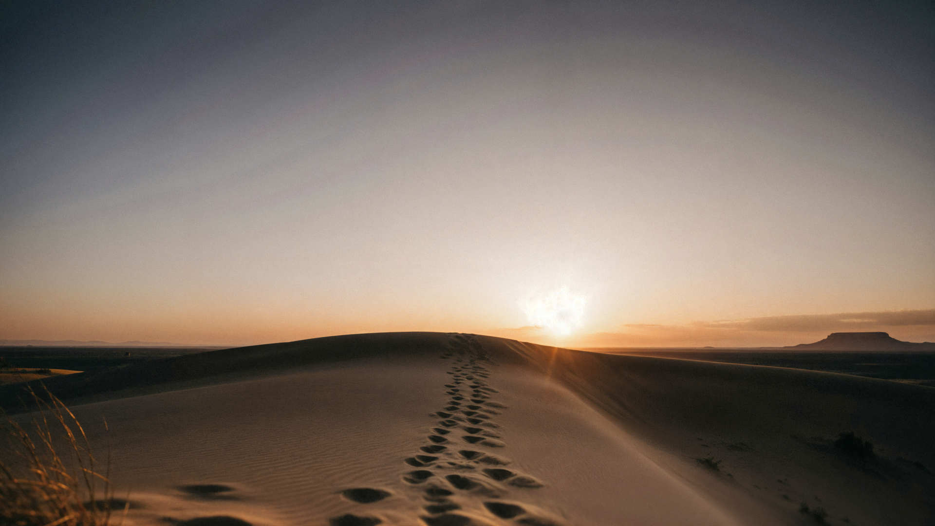 4K Ultra HD PC desktop wallpaper: desert dunes at sunset with long shadows and a trail of footprints leading toward the glowing horizon.