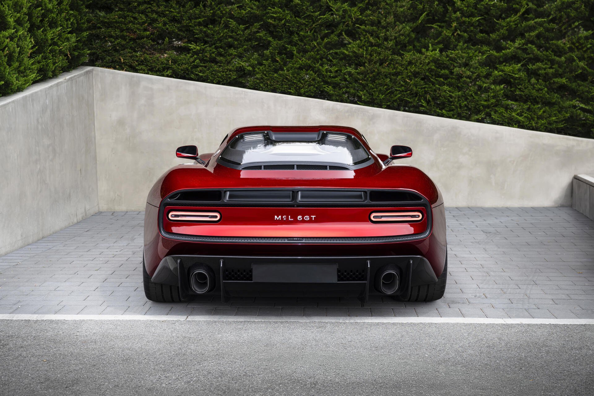 Rear view of a red McLaren McL 6GT sports supercar parked against a concrete wall, rendered as an 8K Ultra HD PC desktop wallpaper/background.