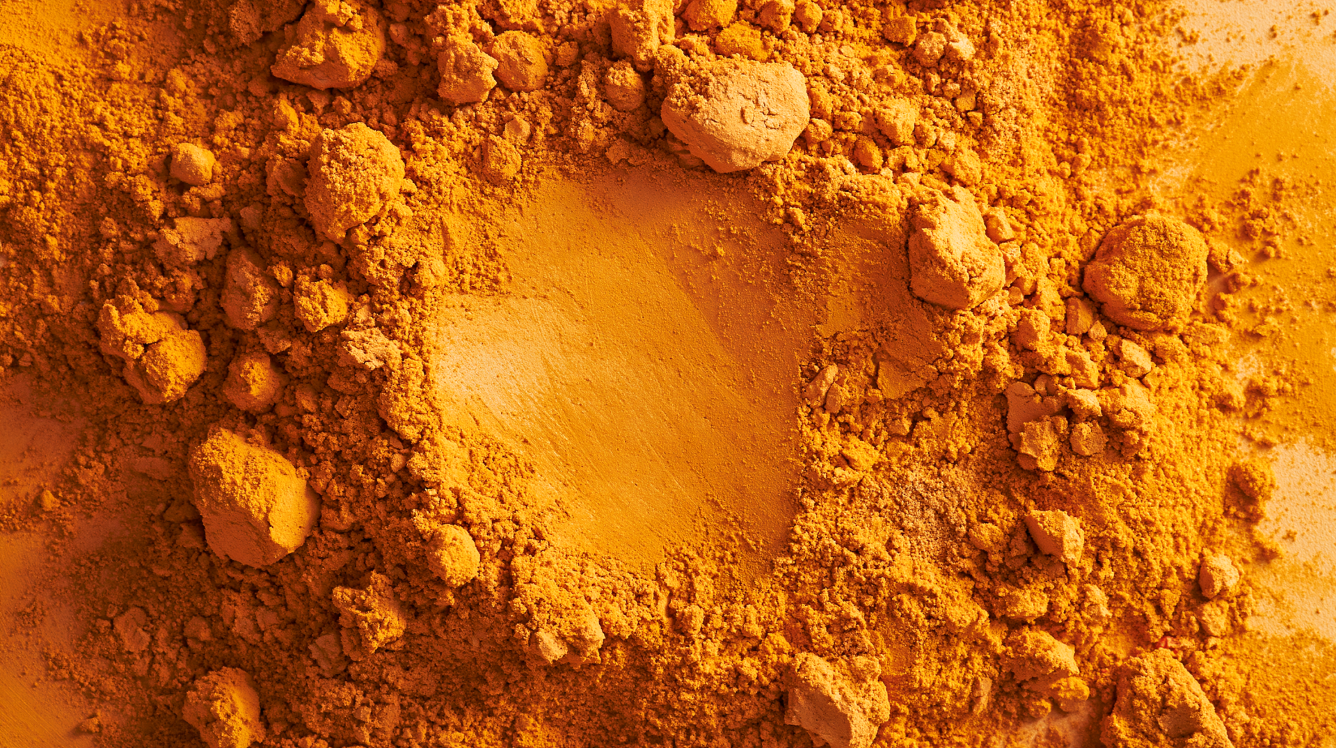 Ochre turmeric spice powder close-up, textured piles and a central scoop; vibrant golden-ocre colors. 2K Quad HD PC desktop wallpaper background.