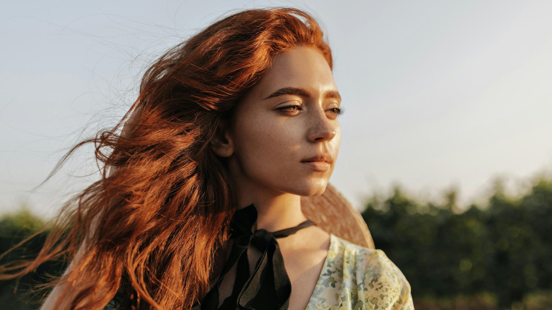 Portrait of a red‑haired girl model gazing toward sunset; 4K Ultra HD PC desktop wallpaper and background with warm golden‑hour light and soft bokeh.