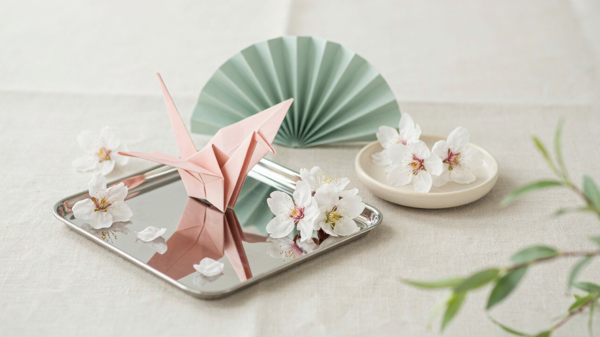 2K Quad HD spring aesthetic desktop wallpaper: pink origami crane and paper flowers on a mirrored tray with a mint paper fan against a soft neutral backdrop.