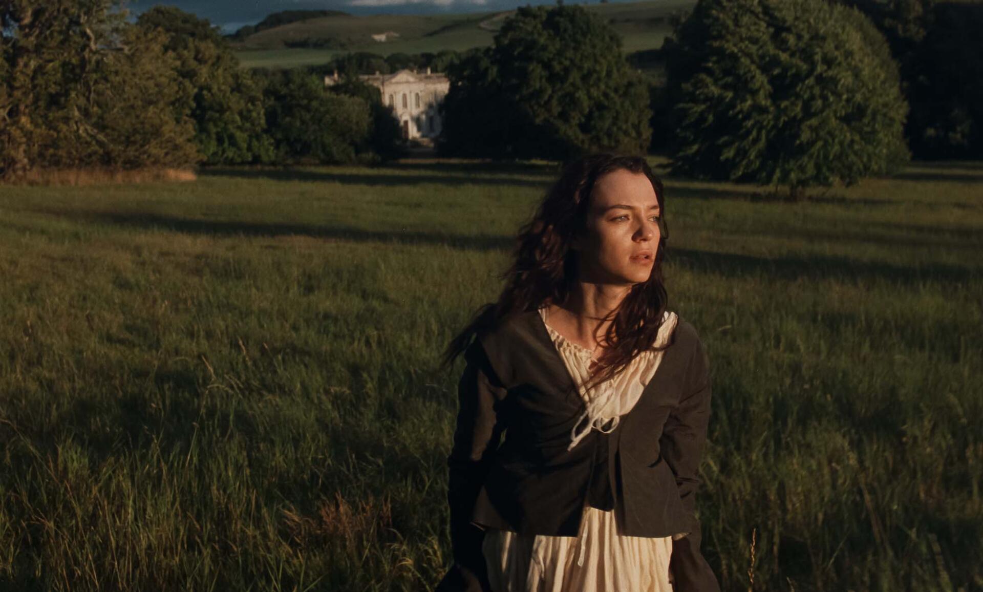 Daisy Edgar-Jones in Sense and Sensibility stands in a sunlit countryside meadow, with a grand estate in the distance—HD desktop wallpaper.