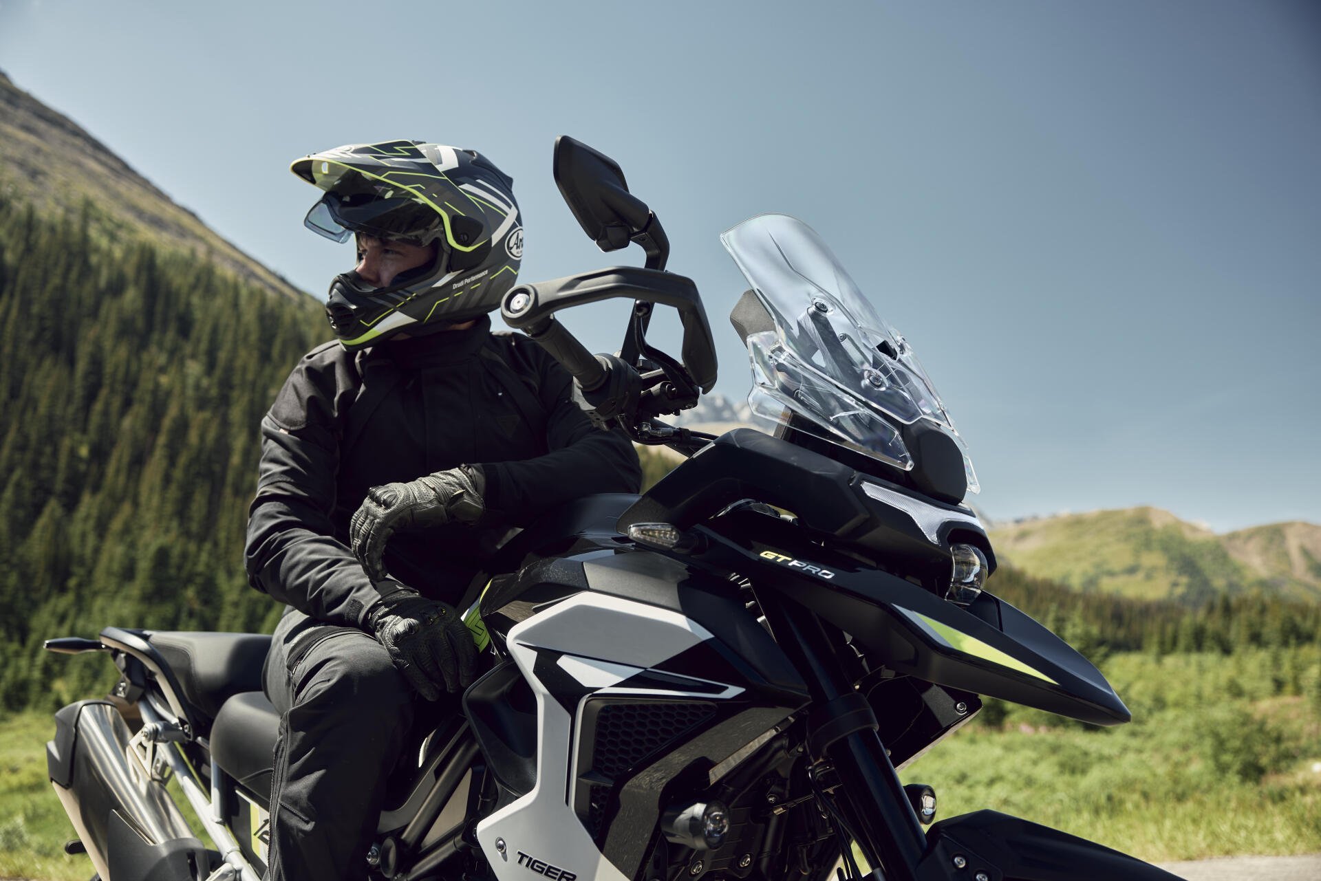 Helmeted motorcyclist riding a Triumph Tiger 1200 through a scenic mountain landscape, featured in 8K Ultra HD PC desktop wallpaper.