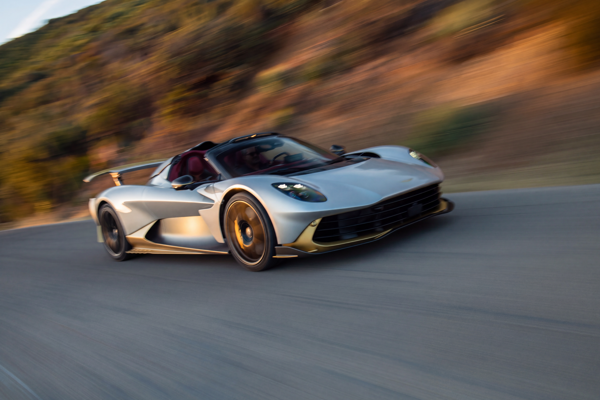 Silver Aston Martin Valhalla Spider supercar racing along a road, featured in an 8K Ultra HD desktop wallpaper.