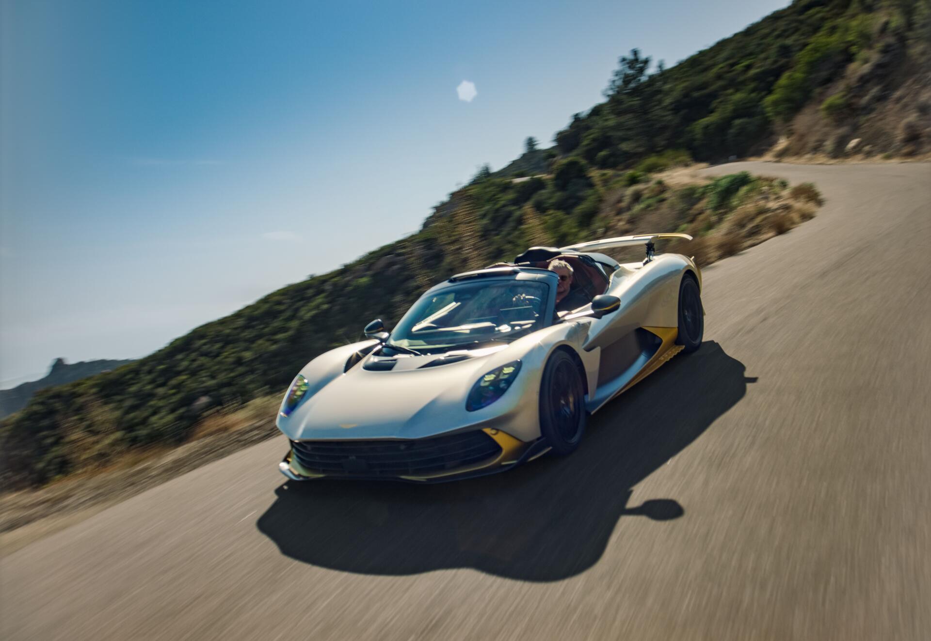 Aston Martin Valhalla Spider sports car racing along a mountain road in an 8K Ultra HD desktop wallpaper.