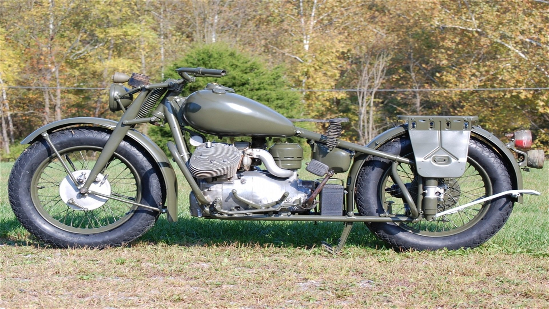HD PC desktop wallpaper featuring a vintage Indian 841 motorcycle parked on grass with a forest backdrop, showcasing its classic military-style design and muted green color.