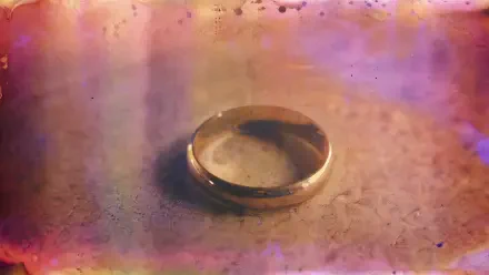 Close-up of a single wedding ring on a textured surface with warm pink and gold bokeh; 4K Ultra HD PC desktop wallpaper and background.