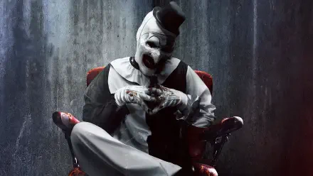 Terrifier 2 4K Ultra HD PC wallpaper: menacing Art the Clown in white makeup and black hat, seated in a red chair, steepling blood-stained fingers against a rain-streaked concrete wall.
