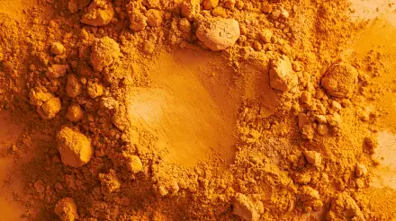 Ochre turmeric spice powder close-up, textured piles and a central scoop; vibrant golden-ocre colors. 2K Quad HD PC desktop wallpaper background.
