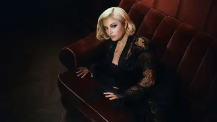 Celebrity singer seated on a velvet sofa in moody lighting, blonde hair and black lace outfit — 4K Ultra HD PC desktop wallpaper/background.