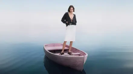 Model stands on a small wooden boat drifting on glassy water, wearing a black jacket and white skirt — 4K Ultra HD PC desktop wallpaper.