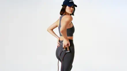 5K Ultra HD PC wallpaper of a woman in dark athletic wear and cap, side pose holding a jump rope against a clean, light background.