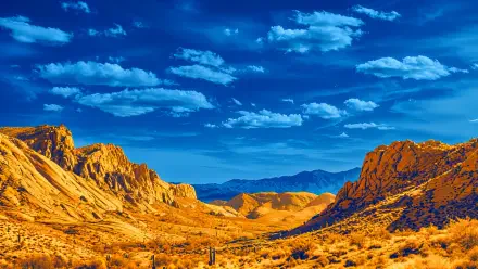 4K Ultra HD desktop wallpaper of a desert mountain landscape: golden rocky hills and scrub under a vivid blue sky with scattered clouds.