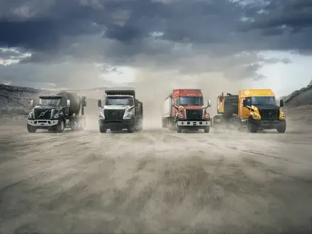 Volvo VNX semi trucks lineup on a dusty road beneath storm clouds, 5K Ultra HD PC desktop wallpaper and background.