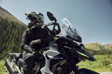 Helmeted motorcyclist riding a Triumph Tiger 1200 through a scenic mountain landscape, featured in 8K Ultra HD PC desktop wallpaper.