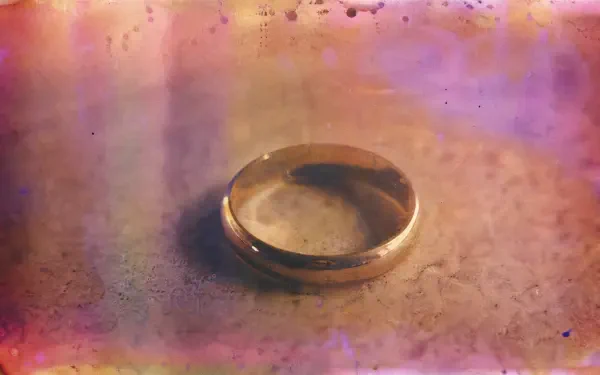 Close-up of a single wedding ring on a textured surface with warm pink and gold bokeh; 4K Ultra HD PC desktop wallpaper and background.