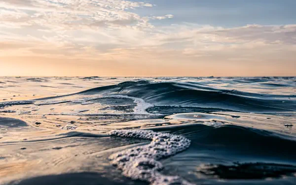 Close-up ocean waves under a pastel sunrise along the distant horizon — 4K Ultra HD PC desktop wallpaper.