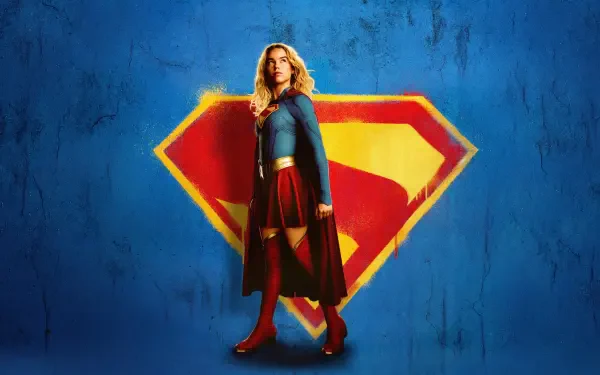 Supergirl (2026) stands in a heroic pose before a large S emblem on a blue textured wall — 4K Ultra HD PC desktop wallpaper.