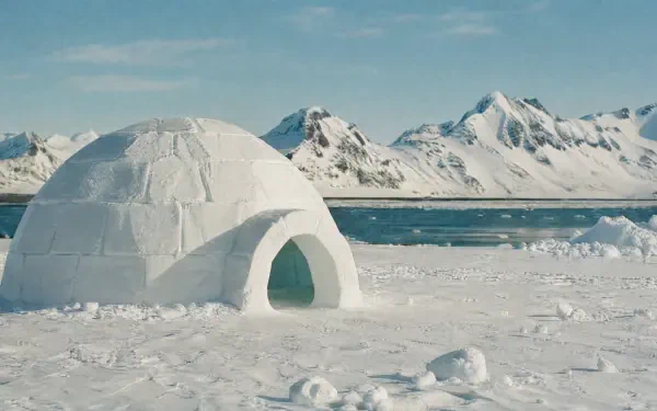 Igloo on a frozen shoreline with distant snow-capped mountains and clear blue sky — 4K Ultra HD PC desktop wallpaper and background.