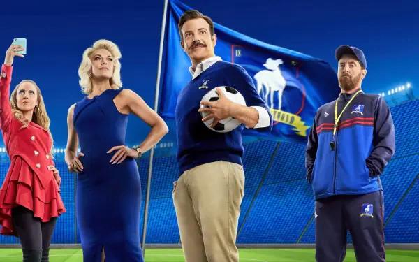 Ted Lasso cast posing in a stadium, central coach with a mustache holding a soccer ball against vivid blue banners — 4K Ultra HD PC desktop wallpaper and background.