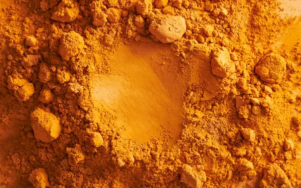 Ochre turmeric spice powder close-up, textured piles and a central scoop; vibrant golden-ocre colors. 2K Quad HD PC desktop wallpaper background.