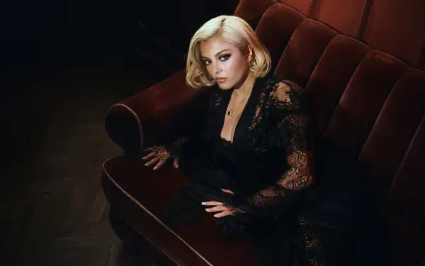 Celebrity singer seated on a velvet sofa in moody lighting, blonde hair and black lace outfit — 4K Ultra HD PC desktop wallpaper/background.