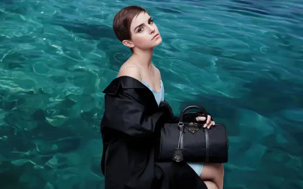4K Ultra HD desktop wallpaper: short-haired woman in a black coat seated by clear turquoise water, gazing upward while holding a structured black handbag.