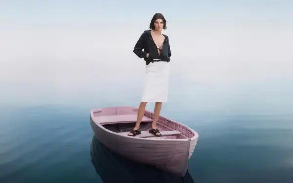 Model stands on a small wooden boat drifting on glassy water, wearing a black jacket and white skirt — 4K Ultra HD PC desktop wallpaper.
