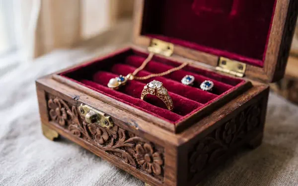 Ornate carved wooden jewelry box with red velvet lining holding a diamond ring and gemstone earrings — 5K Ultra HD PC desktop wallpaper and background.