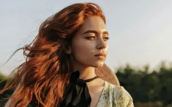 Portrait of a red‑haired girl model gazing toward sunset; 4K Ultra HD PC desktop wallpaper and background with warm golden‑hour light and soft bokeh.