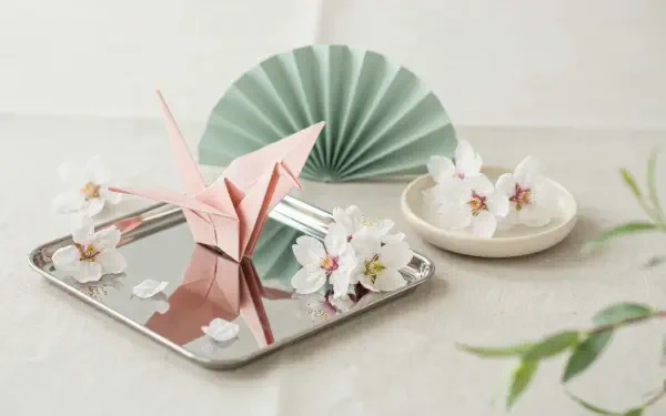 2K Quad HD spring aesthetic desktop wallpaper: pink origami crane and paper flowers on a mirrored tray with a mint paper fan against a soft neutral backdrop.