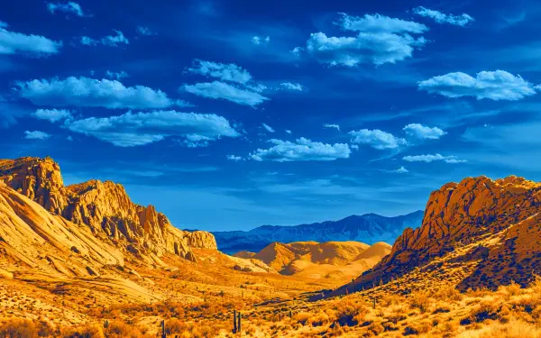 4K Ultra HD desktop wallpaper of a desert mountain landscape: golden rocky hills and scrub under a vivid blue sky with scattered clouds.