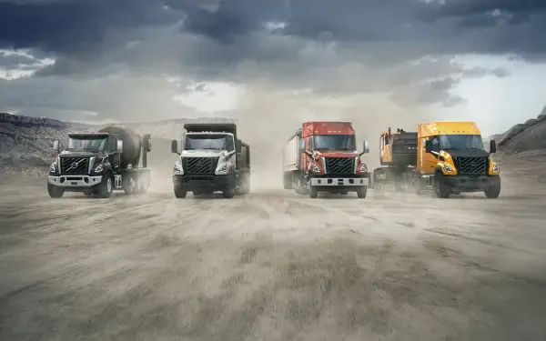 Volvo VNX semi trucks lineup on a dusty road beneath storm clouds, 5K Ultra HD PC desktop wallpaper and background.